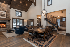Elegant barndominium dining and living area with high ceilings, a stone fireplace, and rustic wood finishes, offering a perfect blend of comfort and sophistication.