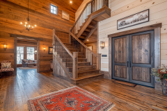 Elegant barndominium entryway with rustic wood accents, a grand staircase, and warm lighting, creating a welcoming farmhouse-style ambiance.