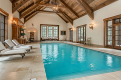Bright and airy barndominium interior featuring a luxurious indoor pool, vaulted wood beam ceiling, and elegant French doors for a timeless retreat.