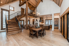 Rustic barndominium interior with a grand wooden staircase, exposed beams, a cozy dining area, and a warm open-concept kitchen.