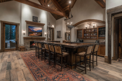 A luxurious barndominium interior featuring a rustic home bar with high ceilings, exposed beams, and warm lighting for a cozy yet elegant ambiance.
