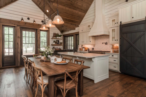 A beautifully designed barndominium kitchen with vaulted wood ceilings, shiplap walls, rustic farmhouse decor, a large dining table, and a black sliding barn door.