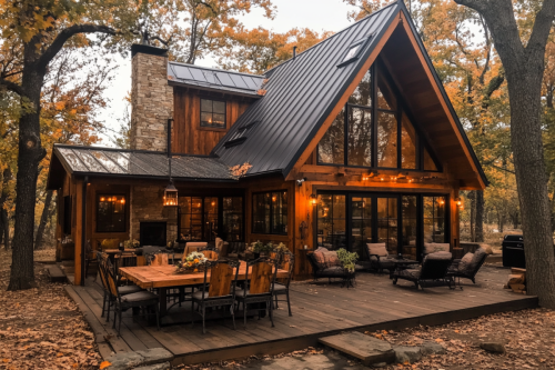 A stunning rustic barndominium with an A-frame design, large windows, a spacious outdoor deck, and warm lighting, set in a wooded autumn landscape.